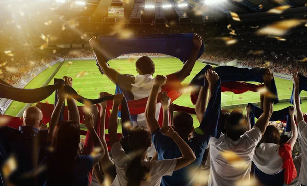 Wygraj. Tylny widok piłki nożnej, kibice kibicują drużynie flagami stanowymi i szalikami na zatłoczonym stadionie w godzinach wieczornych. Koncepcja sportu, wsparcia, rywalizacji. Efekt nieostry — Zdjęcie stockowe
