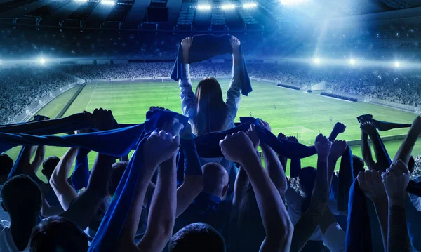 Back view of football, soccer fans cheering their team with scarfs at crowded stadium at evening time. Concept of sport, support, competition. Out of focus effect — Stock Photo, Image