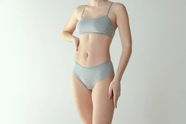 Ausgeschnittene Studioaufnahme eines zarten schlanken weiblichen Körpers in bequemer Unterwäsche isoliert über grauem Hintergrund — Stockfoto