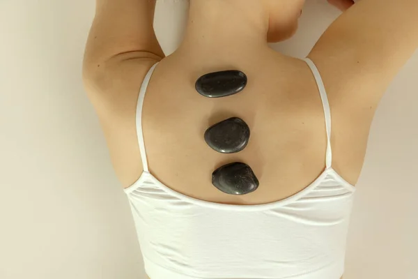 Imagem recortada de costas femininas com pedras isoladas sobre fundo de estúdio cinza. Spa, conceito de massagem — Fotografia de Stock