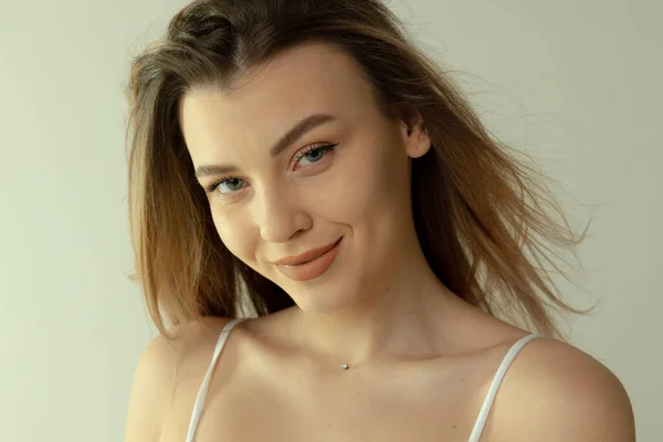 Retrato de cerca de una hermosa joven rubia con maquillaje natural posando aislada sobre un fondo gris de estudio. Sonriendo tiernamente — Foto de Stock