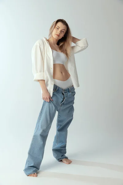 Full-length portret van jong slank meisje dragen shirt, ondergoed en jeans geïsoleerd over grijze studio achtergrond. Jeugdschoonheid — Stockfoto