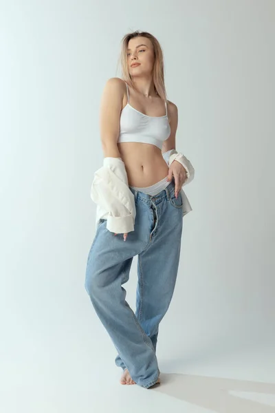 Fullständigt porträtt av ung smal flicka bär skjorta, underkläder och jeans isolerad över grå studio bakgrund — Stockfoto