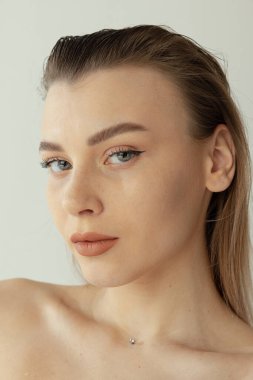 Sarışın ve doğal makyajlı güzel bir kadının yakın plan portresi gri stüdyo arka planında izole edilmiş.