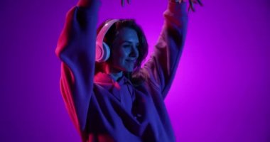 Mutlu gülümseyen genç kız kulaklıkla müzik dinliyor ve mor arka planda dans ediyor neon ışıkta, filtrede. 4 bin. Duygular, reklamlar, kültür, gençlik kavramı