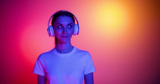 Gelukkig glimlachend jong meisje luisteren naar muziek in koptelefoon en dansen op rood gele achtergrond in neon licht, filter. 4K. Emoties, advertenties, cultuur, jeugdconcept — Stockvideo