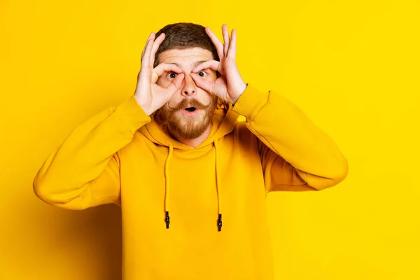 Estudio de disparo de joven loco en sudadera con capucha amarilla haciendo cara, divirtiéndose aislado sobre fondo brillante. Concepto de emociones humanas, expresión facial, ventas, anuncios —  Fotos de Stock