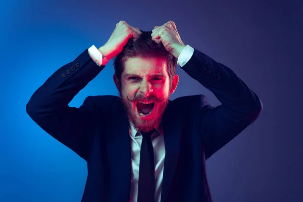 Excited young stylish man in business suit shouting isolated on dark blue studio background. Concept of human emotions, facial expression, sales, ad, fashion and beauty