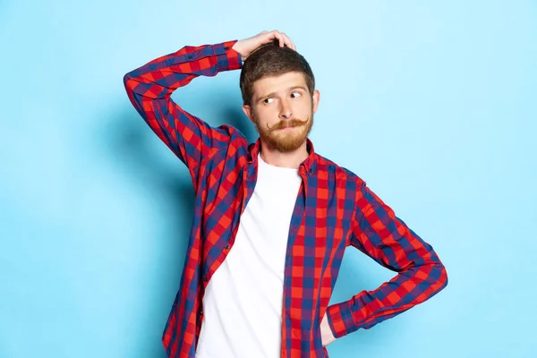 Emozionale giovane uomo con la testa rossa in t-shirt bianca e camicia a quadri posa isolata su sfondo blu. Concetto di arte, moda, emozioni, aspirazione — Foto Stock