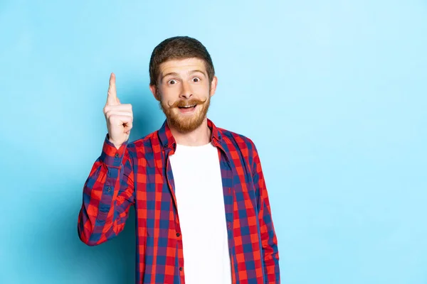 Emotional young red-headed man in white t-shirt and plaid shirt posing isolated on blue background. Concept of art, fashion, emotions, aspiration — Stock Photo, Image