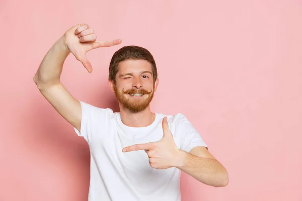Портрет молодого щасливого рудого чоловіка в білій футболці, що позує ізольовано на рожевому фоні. Концепція мистецтва, моди, емоцій, прагнення — стокове фото