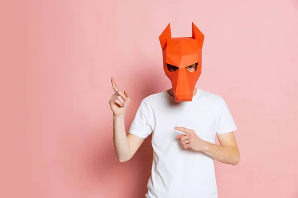 Kreativní portrét mladého muže v bílém tričku s lepenkovou zvířecí maskou na hlavě izolovaný na růžovém pozadí. Koncept umění, módy, divadla, legračních emocí. — Stock fotografie