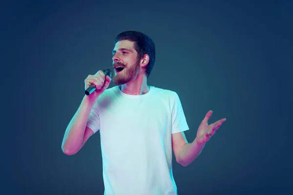 Snygg man i vit t-shirt sång vid mikrofon isolerad på mörkblå studio bakgrund, Begreppet mänskliga känslor, ansiktsuttryck, försäljning, annons, mode och skönhet — Stockfoto