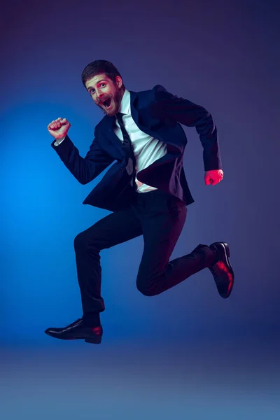 Um jovem homem elegante em terno de negócios pulando isolado no fundo do estúdio azul escuro. Conceito de emoções humanas, expressão facial, vendas, anúncio, moda e beleza — Fotografia de Stock