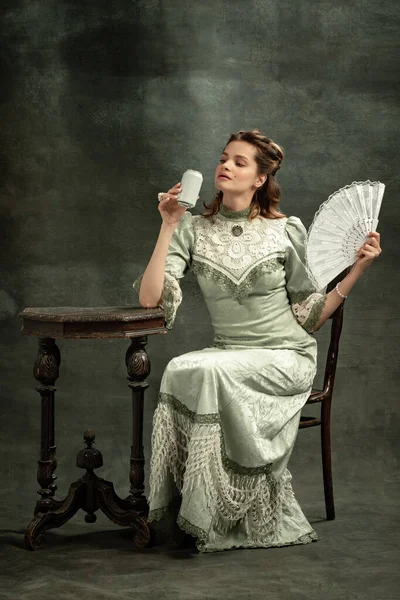 Retrato vintage de una joven hermosa en vestido gris de estilo medieval bebiendo té aislado sobre fondo oscuro. Comparación de conceptos de épocas, estilo flamenco. Arte, belleza — Foto de Stock