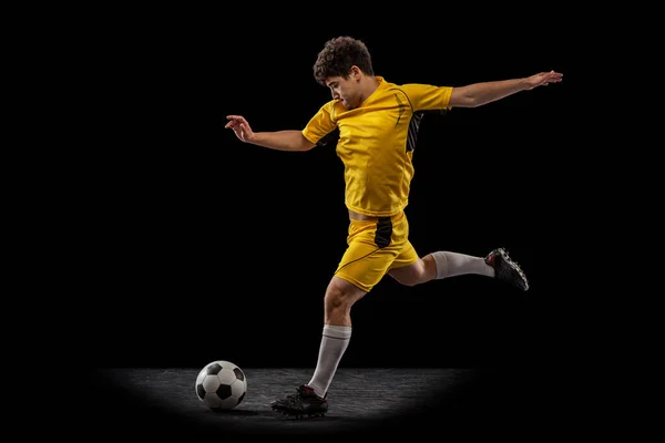 Динамічний портрет професійного футболіста, тренування футболіста з м'ячем ізольовано на темному тлі. Концепція спорту, матч, активний спосіб життя, мета і хобі — стокове фото