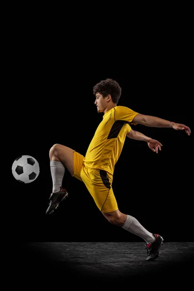 Dynamic portrait of professional football, soccer player training with ball isolated on dark background. Concept of sport, match, active lifestyle, goal and hobby — Stock Photo, Image