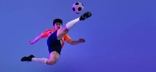 Studio shot van mannelijke professionele voetbal, voetballer oefenen met bal geïsoleerd op paarse achtergrond. Concept sport, match, actieve levensstijl, doel en hobby — Stockfoto