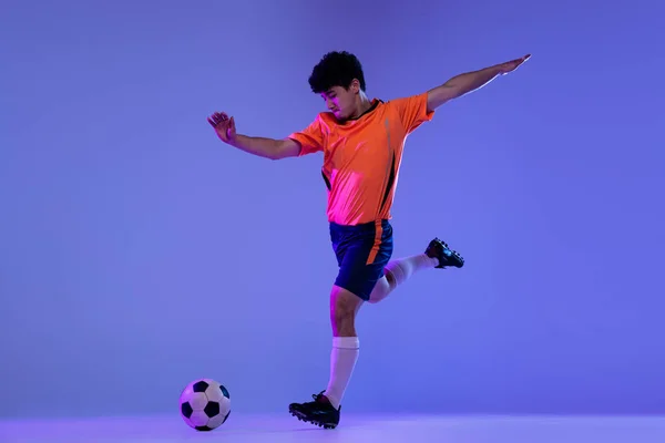 Stúdió lövés férfi profi futball, focista gyakorló labda elszigetelt lila háttér. A sport, mérkőzés, aktív életmód, cél és hobbi fogalma — Stock Fotó