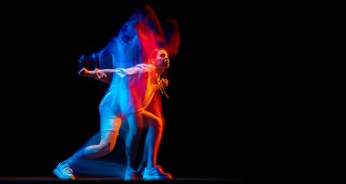 Sportif kıyafetlerle hip-hop dansı yapan genç bir kadın karanlık arka planda karışık neon ışıklarıyla dans ediyor. Gençlik kültürü, hip-hop, hareket
