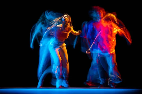 Возбужденные мужчина и женщина танцуют хип-хоп в спортивной одежде на тёмном фоне в танцевальном зале в смешанном неоновом свете. Молодежная культура, хип-хоп, движение — стоковое фото