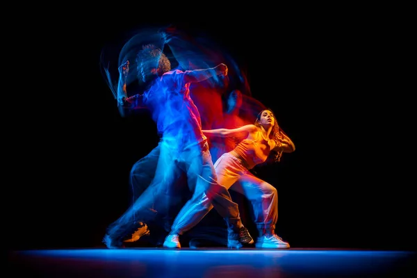 Jovem e mulher dançando hip-hop em roupas de estilo esportivo em fundo escuro no salão de dança em luz de néon misto. Cultura juvenil, hip-hop, movimento — Fotografia de Stock