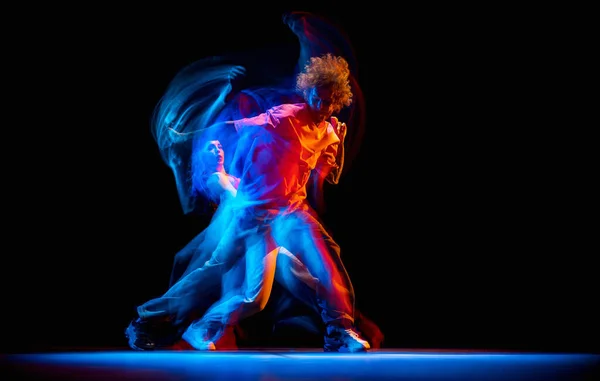 Dynamiczny portret stylowego mężczyzny i dziewczyny tańczące hip-hop w sportowym stylu ubrania na ciemnym tle w sali tanecznej w mieszanym świetle neonowym. Kultura młodzieżowa, breakdance, ruch — Zdjęcie stockowe