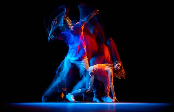 Homem e mulher excitados dançando hip-hop em roupas de estilo esportivo em fundo escuro no salão de dança em luz de néon misto. Cultura juvenil, hip-hop, movimento — Fotografia de Stock