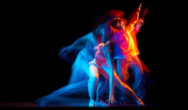 Молодой человек и женщина танцуют хип-хоп в спортивной одежде на тёмном фоне в танцевальном зале в смешанном неоновом свете. Молодежная культура, хип-хоп, движение — стоковое фото