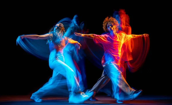 Танцевальное. Гибкие мужчина и девочка, танцоры хип-хопа в движении и действие изолированы на темном фоне в танцевальном зале в синем смешанном неоновом свете. Молодежная культура, хип-хоп, движение — стоковое фото