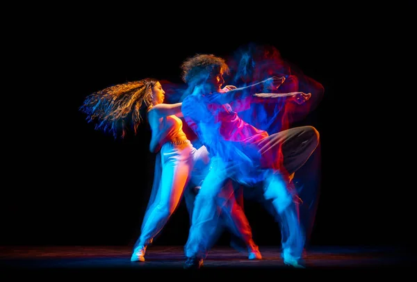 Homme et femme excités dansant hip-hop dans des vêtements de style sportif sur fond sombre à la salle de danse dans la lumière néon mixte. Culture jeunesse, hip-hop, mouvement — Photo