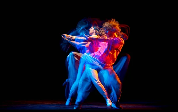 Dynamisch portret van stijlvolle man en meisje dansend hip-hop in sportieve stijl kleding op donkere achtergrond in danszaal in gemengd neonlicht. Jeugdcultuur, breakdance, beweging — Stockfoto