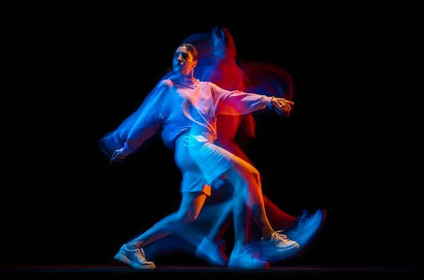 Mladá žena tančí hip-hop ve sportovním stylu oblečení izolované na tmavém pozadí v tanečním sále ve smíšeném neonovém světle. Mládež kultura, hip-hop, hnutí — Stock fotografie
