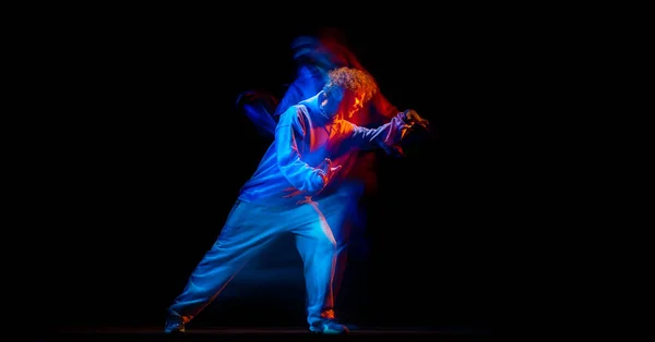 Поразительный мужчина, танцор хип-хопа в спортивной одежде, танцующий на тёмном фоне в танцевальном зале в смешанном неоновом свете. Молодежная культура, хип-хоп, движение — стоковое фото