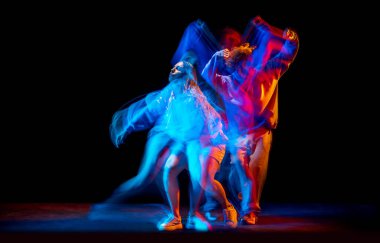 Genç adam ve kadın, karışık neon ışıklarıyla dans salonunun arka planında spor kıyafetleriyle hip-hop dansı yapıyorlar. Gençlik kültürü, hip-hop, hareket