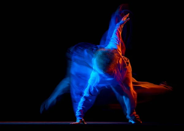 Jonge sportieve man dansend hip-hop in sportieve stijl kleding geïsoleerd op donkere achtergrond in danszaal in gemengd neon licht. Jeugdcultuur, hiphop, beweging — Stockfoto