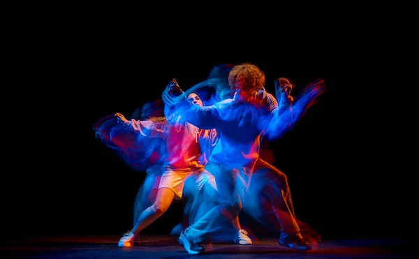 Динамичный портрет стильного мужчины и девушки, танцующих хип-хоп в спортивной одежде на тёмном фоне в танцевальном зале в смешанном неоновом свете. Молодежная культура, брейк-данс, движение — стоковое фото