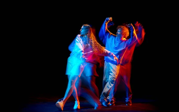 Молодой человек и женщина танцуют хип-хоп в спортивной одежде на тёмном фоне в танцевальном зале в смешанном неоновом свете. Молодежная культура, хип-хоп, движение — стоковое фото