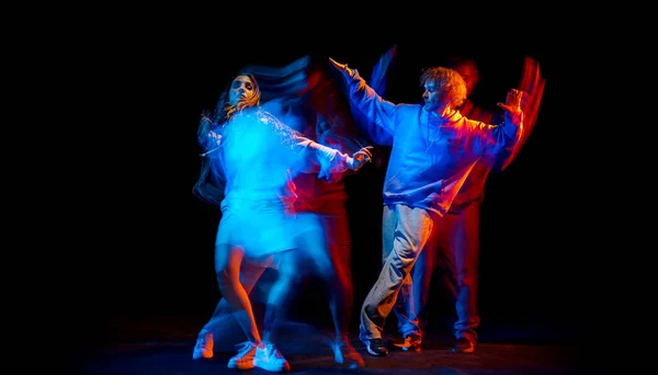 Dance show. Flexible man and girl, hip-hop dancers in motion and action isolated on dark background at dance hall in blue mixed neon light. Youth culture, hip-hop, movement