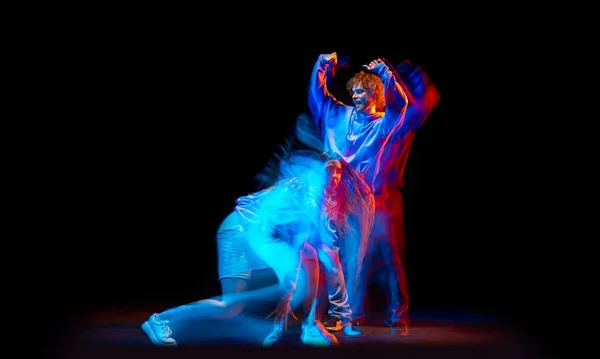 Танцевальное. Гибкие мужчина и девочка, танцоры хип-хопа в движении и действие изолированы на темном фоне в танцевальном зале в синем смешанном неоновом свете. Молодежная культура, хип-хоп, движение — стоковое фото