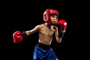 Sportif çocuğun dinamik portresi, boksör eldivenli ve şortlu çocuk koyu arka planda izole edilmiş. Spor, hareket, öğrenim, başarılar, aktif yaşam tarzı kavramı.