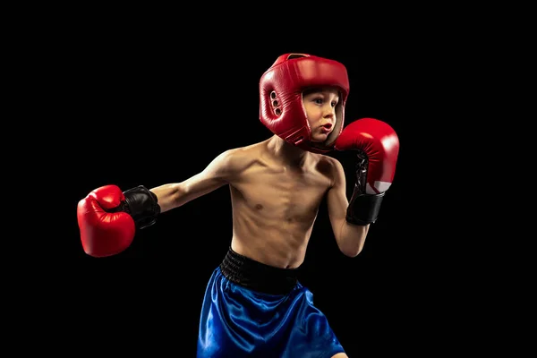Dynamic portrait of sportive boy, kid in boxer gloves and shorts practicing isolated on dark background. Concept of sport, movement, studying, achievements, active lifestyle. — Stock Photo, Image