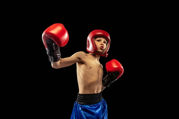 Retrato dinámico de niño deportivo, niño con guantes de boxeador y pantalones cortos practicando aislado sobre fondo oscuro. Concepto de deporte, movimiento, estudio, logros, estilo de vida activo. —  Fotos de Stock