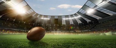 Stadyumdaki futbol sahasının çimlerinde spot ışıklarıyla deri Amerikan futbol topu. Spor, sanat, enerji, güç kavramı
