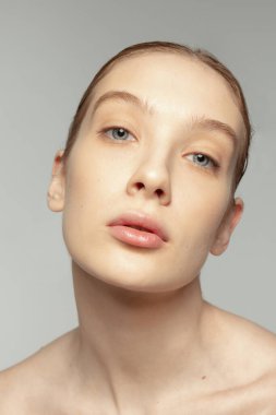 Gri arka planda izole edilmiş pürüzsüz cilde sahip güzel bir kızın yakın plan portresi. Kozmetik yüz temizleme. Güzellik kavramı, doğal ten, kozmetoloji, spa, plastik süphe, tıp