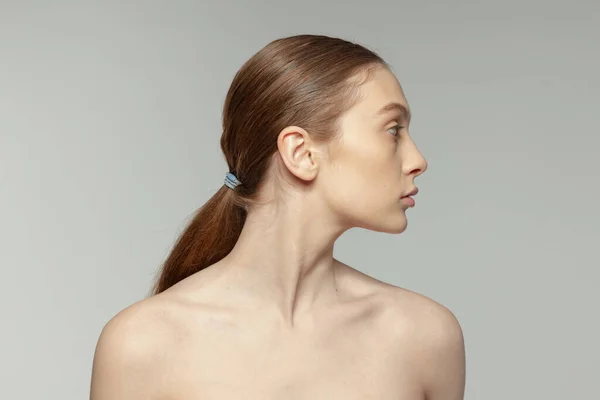 低いポニーテールを持つ若い女の子は グレーのスタジオの背景に隔離されたポーズ 美容の顔の治療 完璧な顔の形 ナチュラルスキン プラスチックサギー 医学の概念 — ストック写真