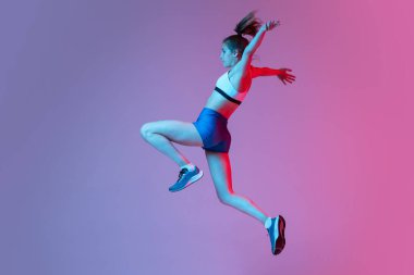 Uzun atlama sporu eğitimi. Genç kız, bayan atlet pembe stüdyo arka planında mavi neon filtresi ve ışık ile izole edilmiş. Eylem kavramı, hareket, hız, sağlıklı yaşam tarzı. Boşluğu kopyala