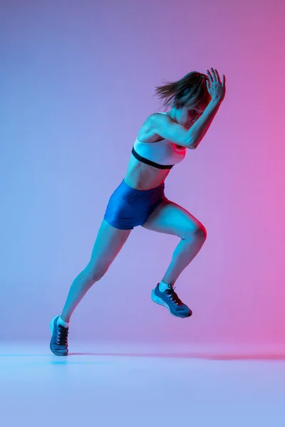 工作室拍摄的专业女运动员 跑步训练孤立在粉红色工作室背景与蓝色霓虹灯过滤器 行动的概念 健康的生活方式 复制空间 — 图库照片