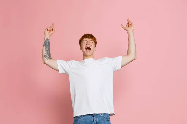 哇哦年轻而兴奋的红头发男子身穿白色T恤 在粉红的工作室背景下显得孤立无援 盖伊怒气冲冲地举起手 面部表情和广告的概念 — 图库照片