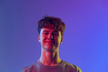 Gülümsüyor. Genç, kızıl saçlı bir adam, mavi stüdyonun arka planında izole edilmiş bir öğrenci. Gençlik kavramı, moda, duygular, yüz ifadesi. İlan için alanı kopyala